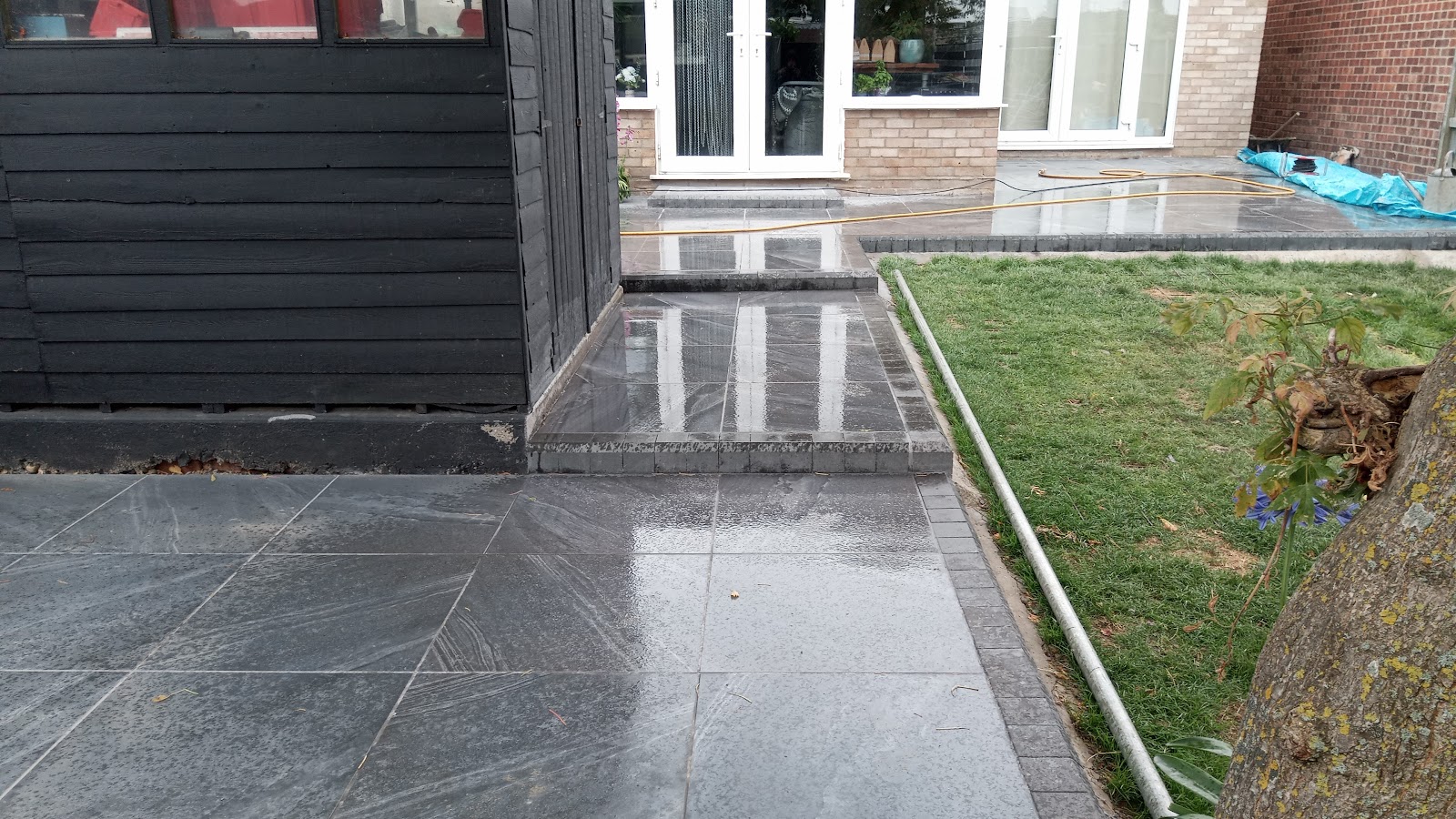 Dark porcelain patio with a strip of new turf after rain